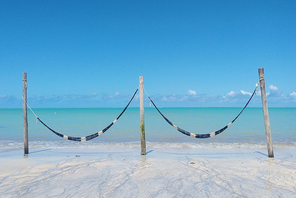 Vista panorâmica da Praia de Barra Grande em Maragogi com águas cristalinas e piscinas naturais e duas redes próximas ao mar.