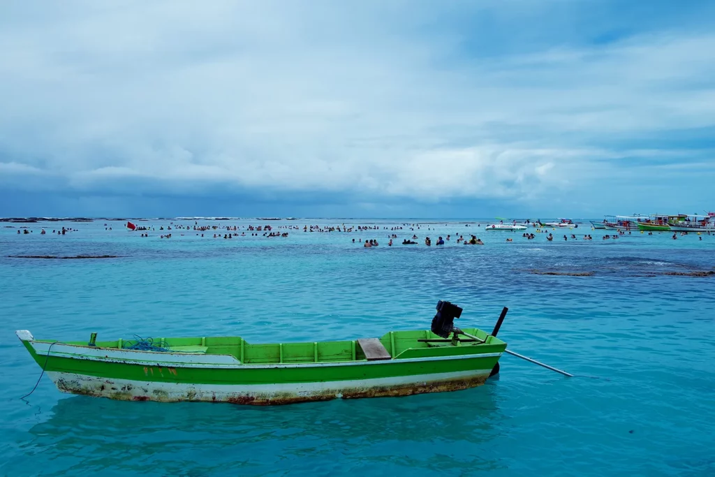 Vista paradisíaca das Praias de Maragogi, com a água azul cristalina, uma canoa mais próxima e pessoas mais ao fundo.