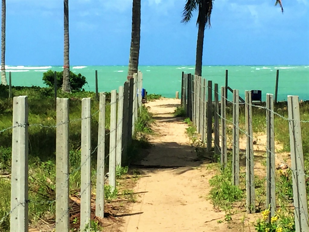 Vista de um caminho cercado que leva à praia em Milagres.